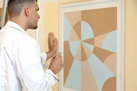 Lehrling vor einer geometrischen Wandgestaltung in Pastelltönen